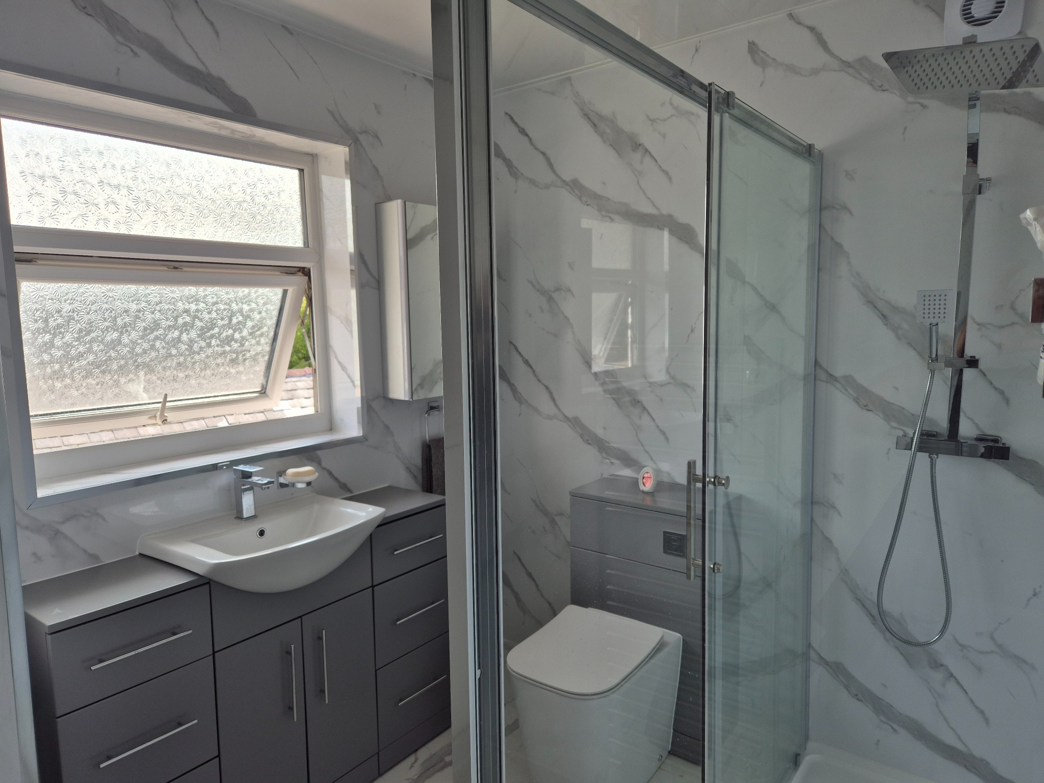 Completed bathroom renovation with walk-in shower, vanity and marble-effect wall panels